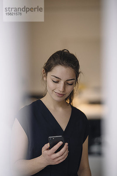 Porträt einer lächelnden jungen Frau  die auf ein Mobiltelefon schaut
