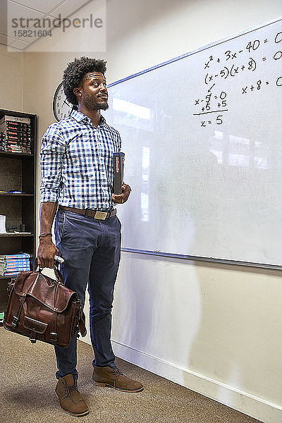 Mathelehrer mit seiner Tasche und seinem Mathebuch vor dem Whiteboard
