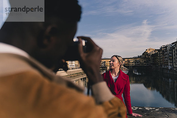 Junger Mann fotografiert seine Freundin auf einer Brücke über dem Arno  Florenz  Italien