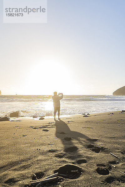 Mann steht bei Sonnenuntergang am Strand und macht Fotos  Sao-Miguel-Insel  Azoren  Portugal