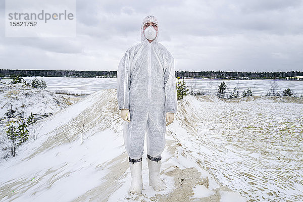 Mann mit Schutzanzug und Maske steht in ländlicher Winterlandschaft