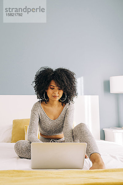 Porträt einer jungen Frau mit lockigem Haar mit Laptop auf dem Bett zu Hause