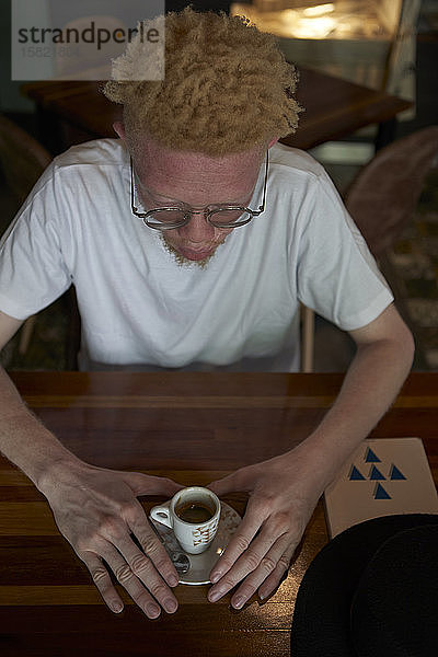 Blick von oben auf einen Albino-Mann  der eine Tasse Kaffee trinkt