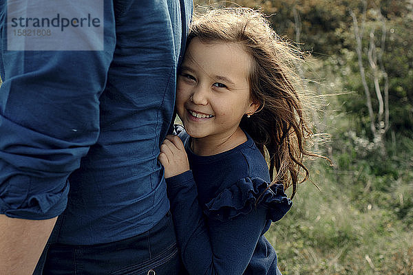 Porträt eines lachenden kleinen Mädchens  das sich hinter dem Rücken seines Vaters versteckt