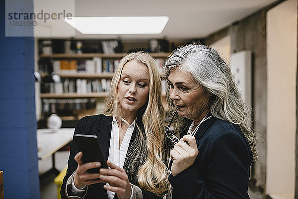 Reife und junge Geschäftsfrau nutzt Smartphone im Loft-Büro