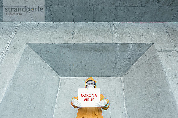 Porträt eines Mannes in Schutzkleidung mit Corona-Virus -Schild