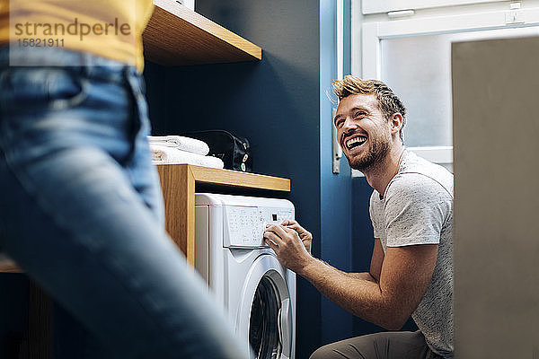 Glücklicher junger Mann  der seine Freundin ansieht und zu Hause die Wäsche wäscht