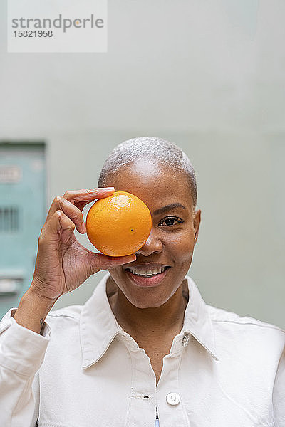 Porträt einer glücklichen Frau  die im Freien ihr Auge mit einer Orange bedeckt