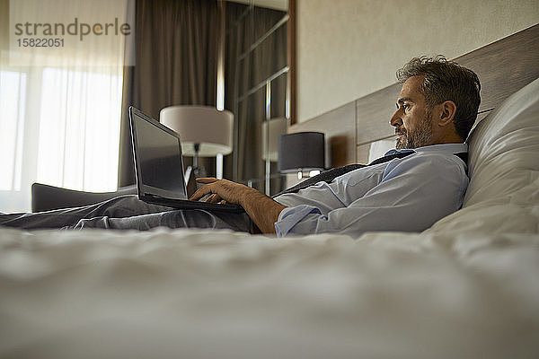 Geschäftsmann im Hotelzimmer auf dem Bett liegend mit Laptop