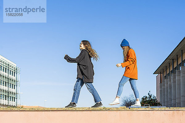 Zwei Teenager-Mädchen laufen auf einer Mauer gegen den Himmel