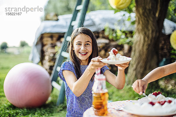 Porträt eines glücklichen Mädchens  das auf einer Geburtstagsfeier im Freien ein Stück Kuchen erhält