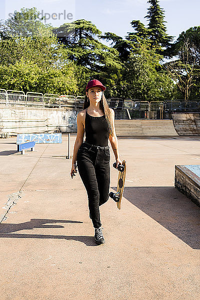 Junge Frau mit Skateboard und Smartphone in einem Skatepark