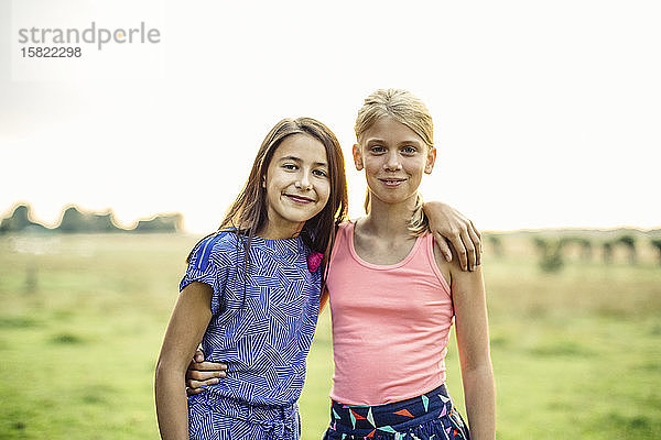 Porträt von zwei lächelnden Mädchen  die sich auf einem Feld umarmen