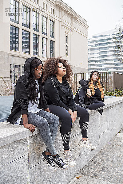 Drei sportliche junge Frauen sitzen auf einer Mauer in der Stadt