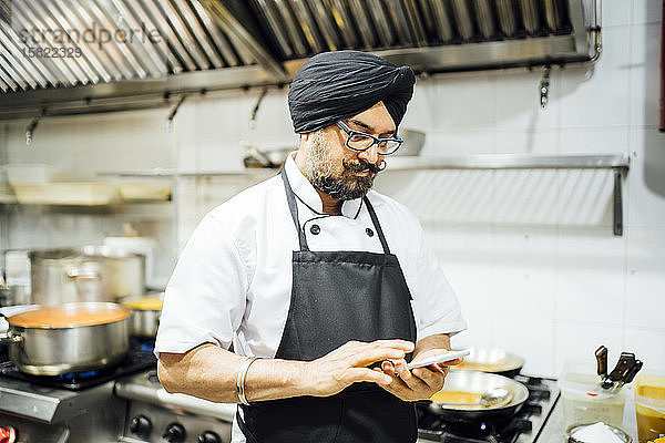 Indischer Küchenchef benutzt Smartphone in Restaurantküche