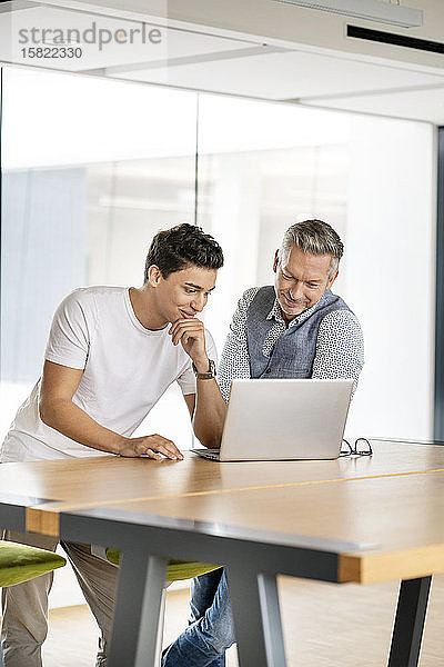 Ein älterer Geschäftsmann arbeitet mit einem jungen Kollegen zusammen und benutzt einen Laptop