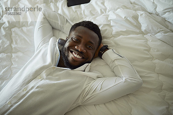 Porträt eines glücklichen Mannes in weißem Hemd im Bett liegend