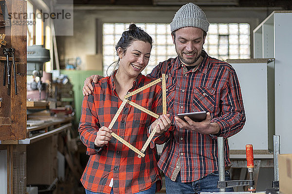 Porträt einer glücklichen Handwerkerin und eines Handwerkers  die in ihrer Werkstatt Tafel und Messlatte halten