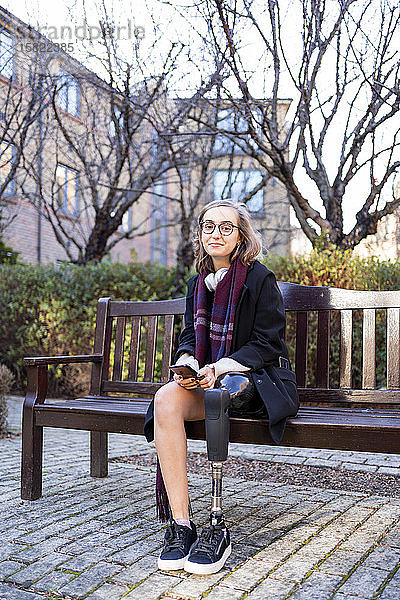 Porträt einer selbstbewussten jungen Frau mit Beinprothese  die auf einer Bank in der Stadt sitzt