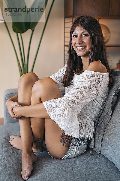 Porträt einer lächelnden jungen Frau  die zu Hause auf der Couch sitzt