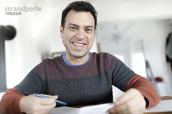 Porträt eines lächelnden reifen Mannes mit Dokumenten  der zu Hause am Tisch sitzt