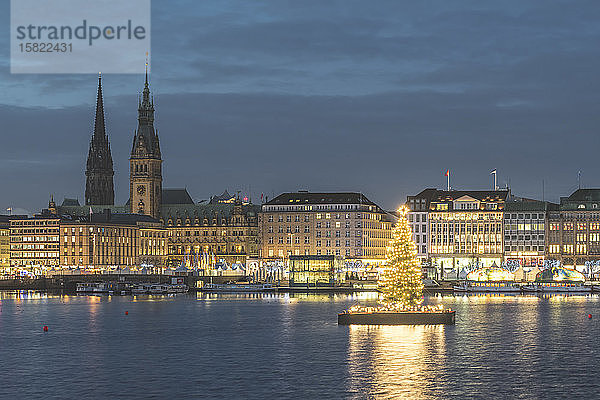 Deutschland  Hamburg  Beleuchteter Alstertanne-Baum in der Abenddämmerung mit Jungfernstieg-Promenade und Nikolauskirche im Hintergrund
