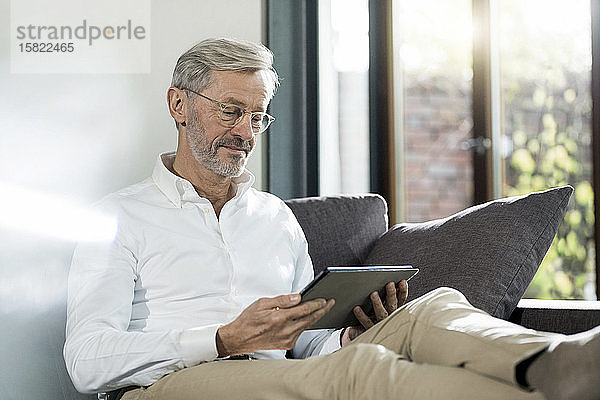 Älterer Mann mit grauen Haaren in modernem Design-Wohnzimmer auf Couch sitzend mit Tablett