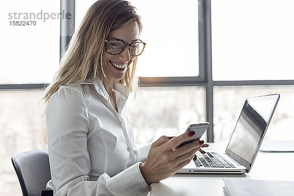 Geschäftsfrau  die im Büro sitzt und am Laptop arbeitet  mit einem Smartphone