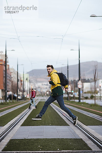 Mann mit Rucksack in der Stadt springt auf Straßenbahnschienen