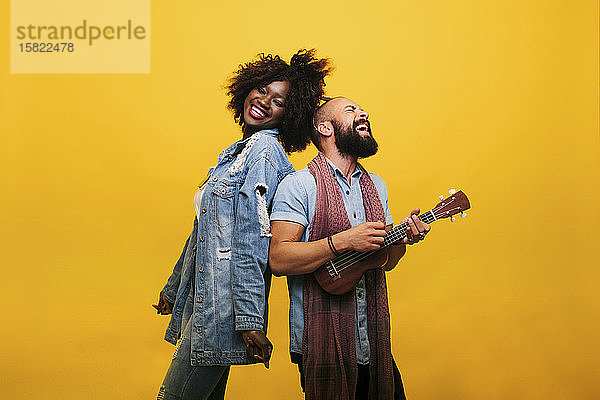 Glücklicher junger Mann mit Frau im Studio beim Ukulele spielen