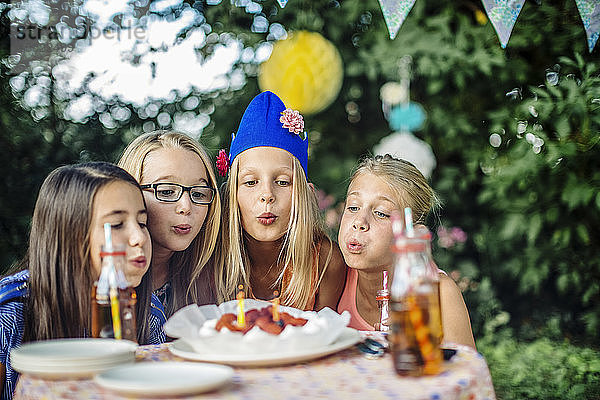 Mädchen feiern eine Geburtstagsparty im Freien und blasen Kerzen auf dem Kuchen aus