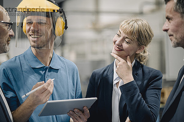 Geschäftsleute und lächelnder Arbeiter mit Tabletten im Gespräch in einer Fabrik