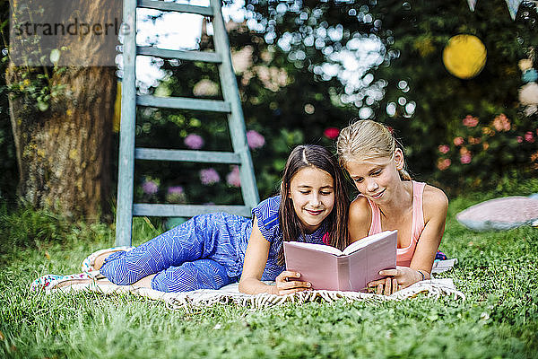 Lächelnde Mädchen lesen gemeinsam ein Buch im Garten