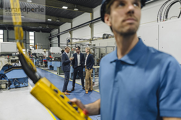 Geschäftsleute bei einer Besprechung in einer Fabrik mit der Arbeitermaschine im Vordergrund