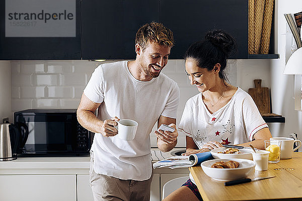 Glückliches junges Paar in der Küche  das auf sein Handy schaut