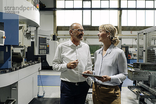 Mann und Frau mit Tablette im Gespräch in einer Fabrik