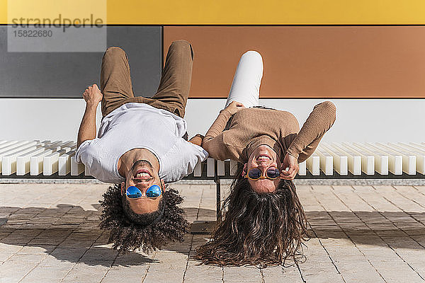 Paar mit Sonnenbrille  auf der Bank entspannen  auf dem Rücken liegend  Köpfe herunterhängen