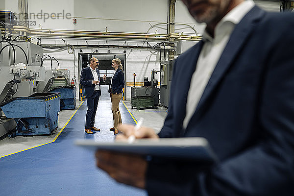 Geschäftsmann mit Tablette in einer Fabrik mit Kollegen im Hintergrund