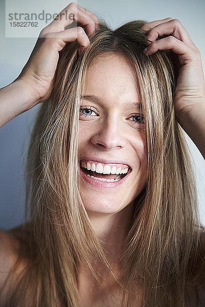 Porträt einer lachenden blonden jungen Frau mit Händen im Haar