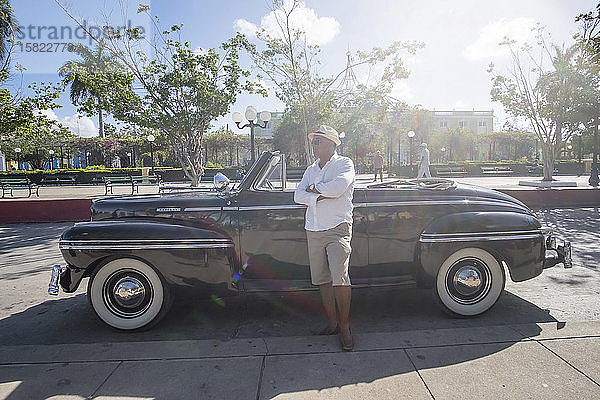 Taxifahrer  der neben einem Oldtimer-Cabriolet steht  Trinidad  Kuba