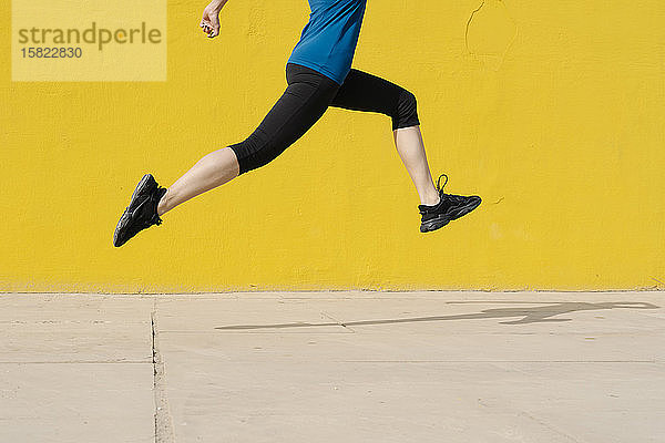 Junge Frau joggt vor einer gelben Wand