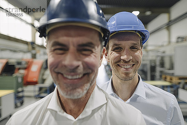 Porträt von zwei lächelnden Männern mit Schutzhelmen in einer Fabrik