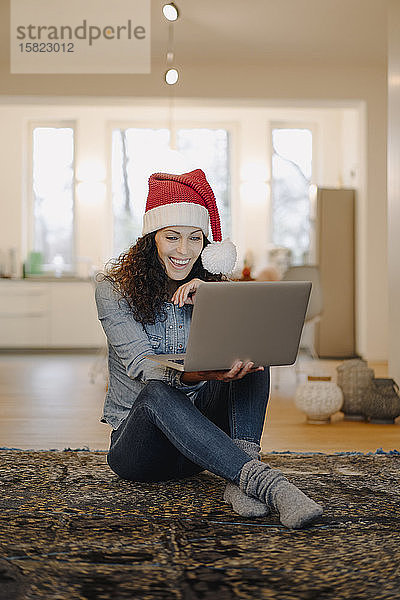 Frau mit Weihnachtsmannmütze sucht online nach Geschenken  mit Laptop