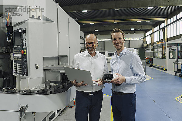 Porträt von zwei lächelnden Männern in einer Fabrik mit Laptop und VR-Brille
