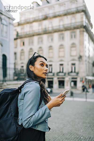 Porträt einer jungen Frau mit Rucksack und Smartphone  die etwas beobachtet  Lissabon  Portugal