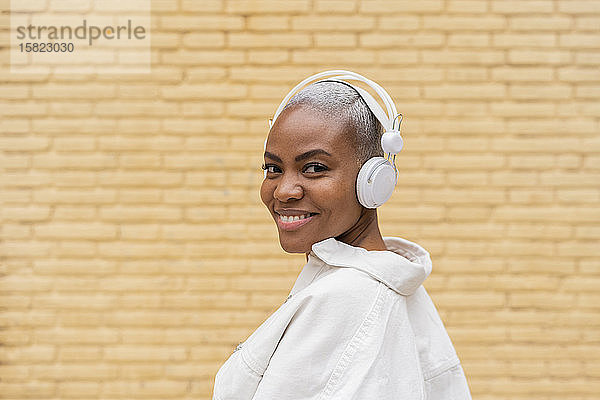 Porträt einer lächelnden Frau  die im Freien mit Kopfhörern Musik hört
