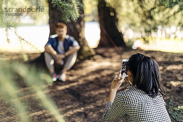 Junge Frau macht Handyfoto von ihrem Freund unter einem Baum