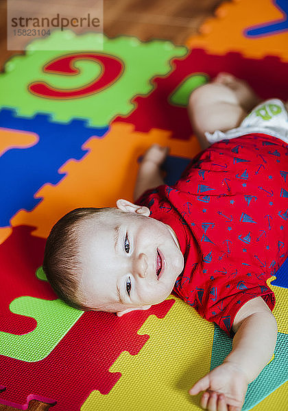 Porträt eines lächelnden kleinen Jungen  der auf einem bunten Boden liegt