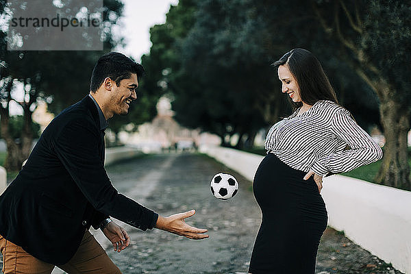 Glückliche werdende Eltern spielen mit einem Ball