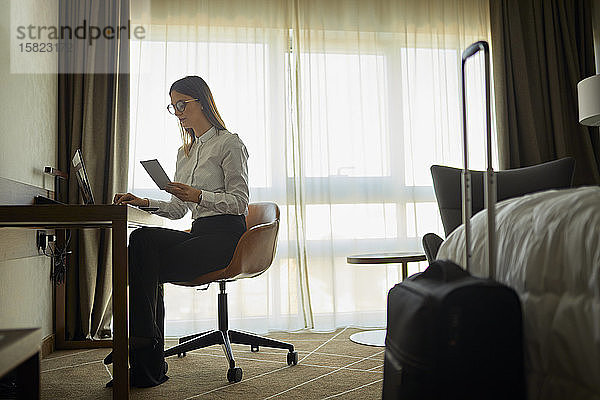 Geschäftsfrau sitzt mit Laptop am Schreibtisch im Hotelzimmer
